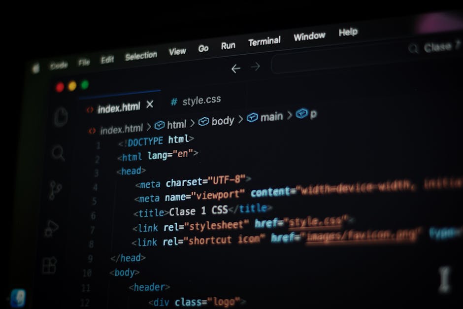 A close-up of a laptop sitting on a grey surface displaying a dark-themed code editor with lines of JavaScript or React code, including HTML tags and functions, related to web development. The screen 