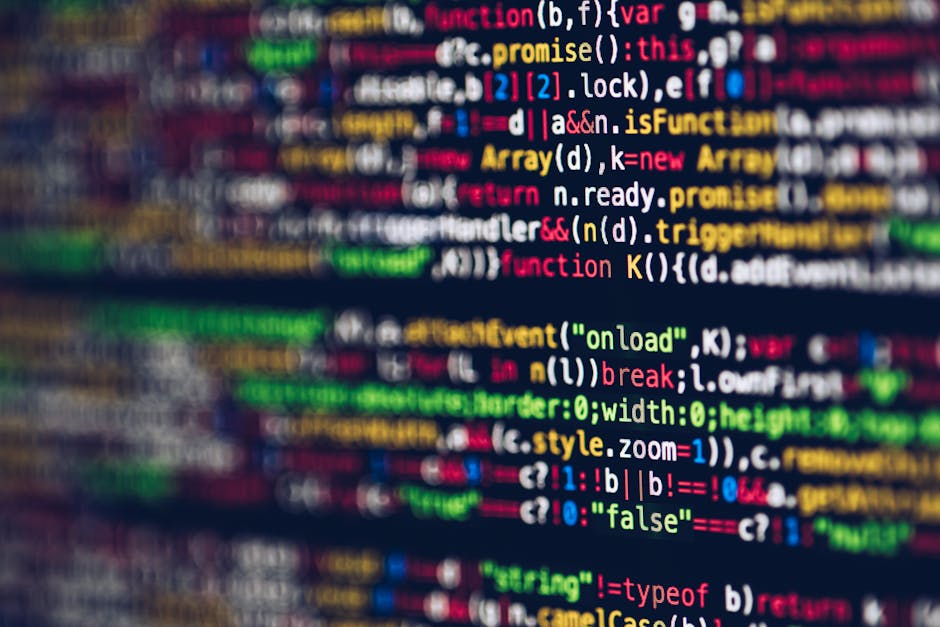 A close-up view of a person's hand typing on a silver laptop keyboard, which is placed on a wooden surface. The laptop screen displays lines of code with syntax highlighting in different colours. The 